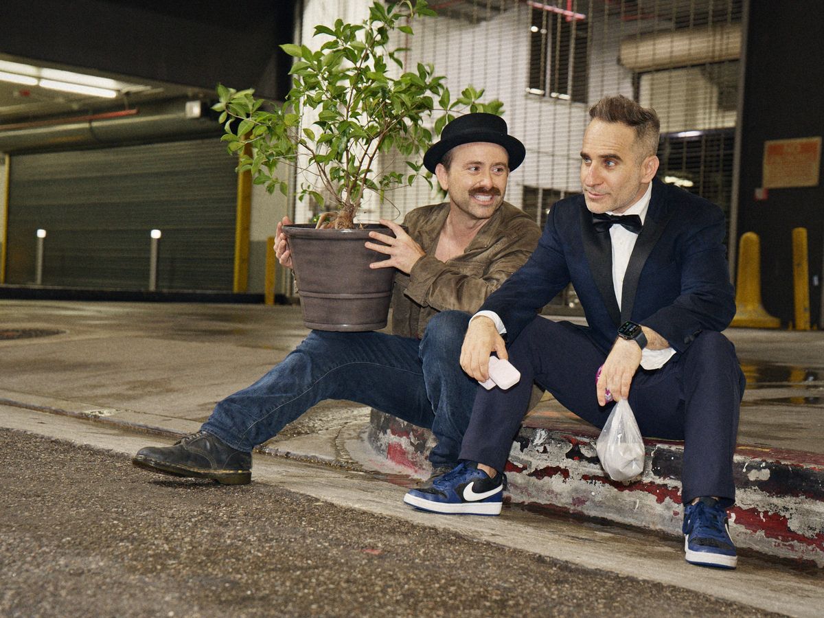 Ben Giroux and Arnie Pantoja sitting on a curb with a potted plant